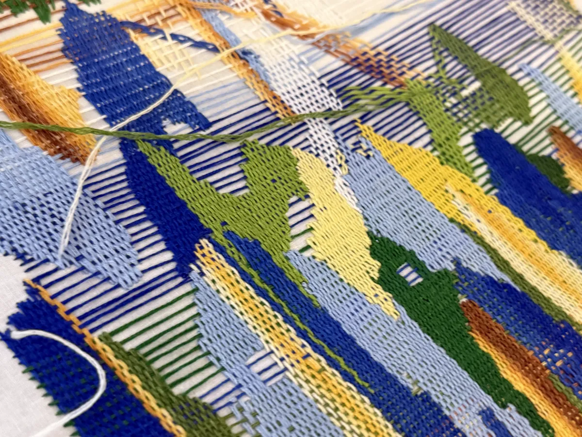 Close-up of a weaving: floats of cobalt, sky blue, green, yellow and ochre threads over a white warp.