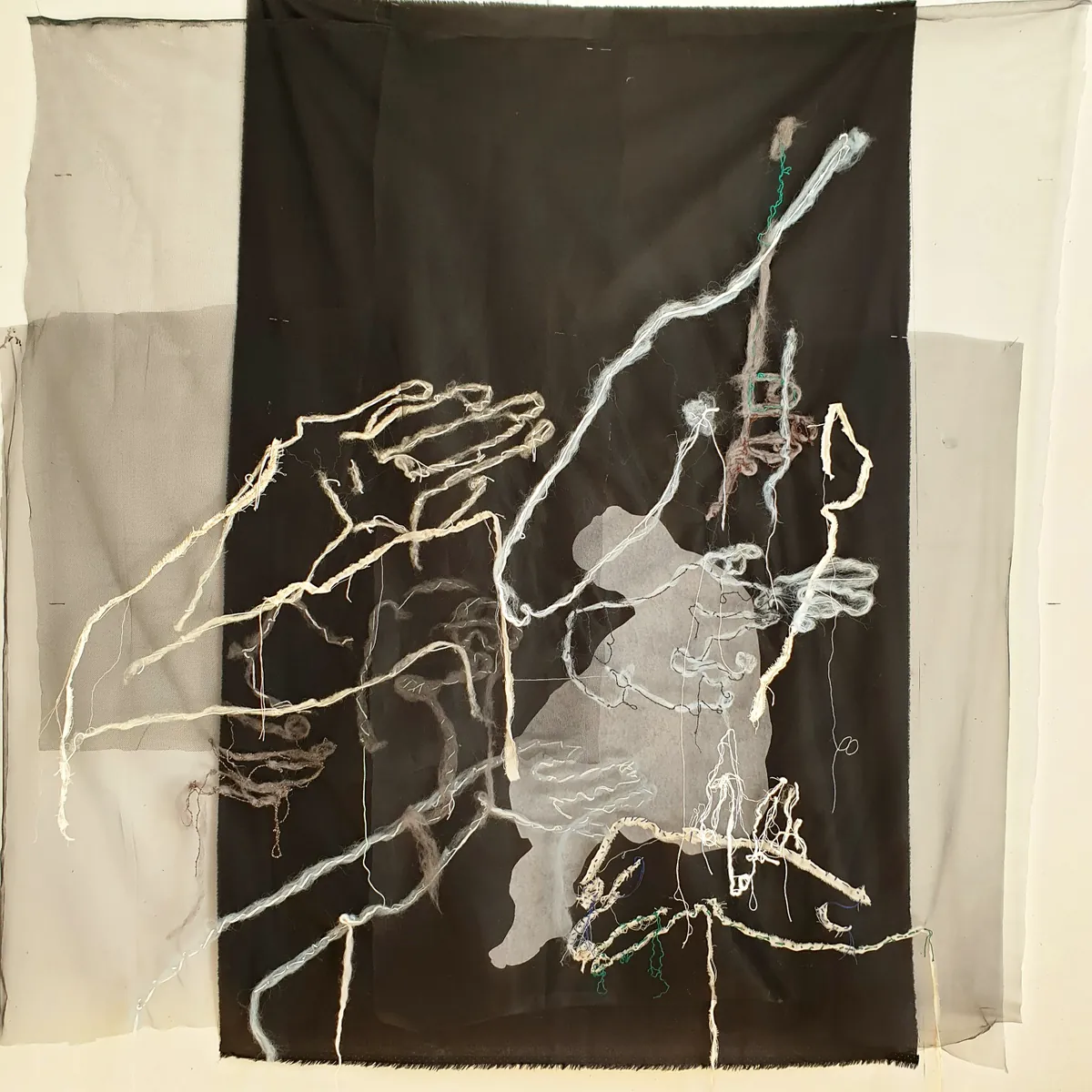 On black cloth framed by grey tulle, twisted white and grey yarns trace the outlines of reaching hands.